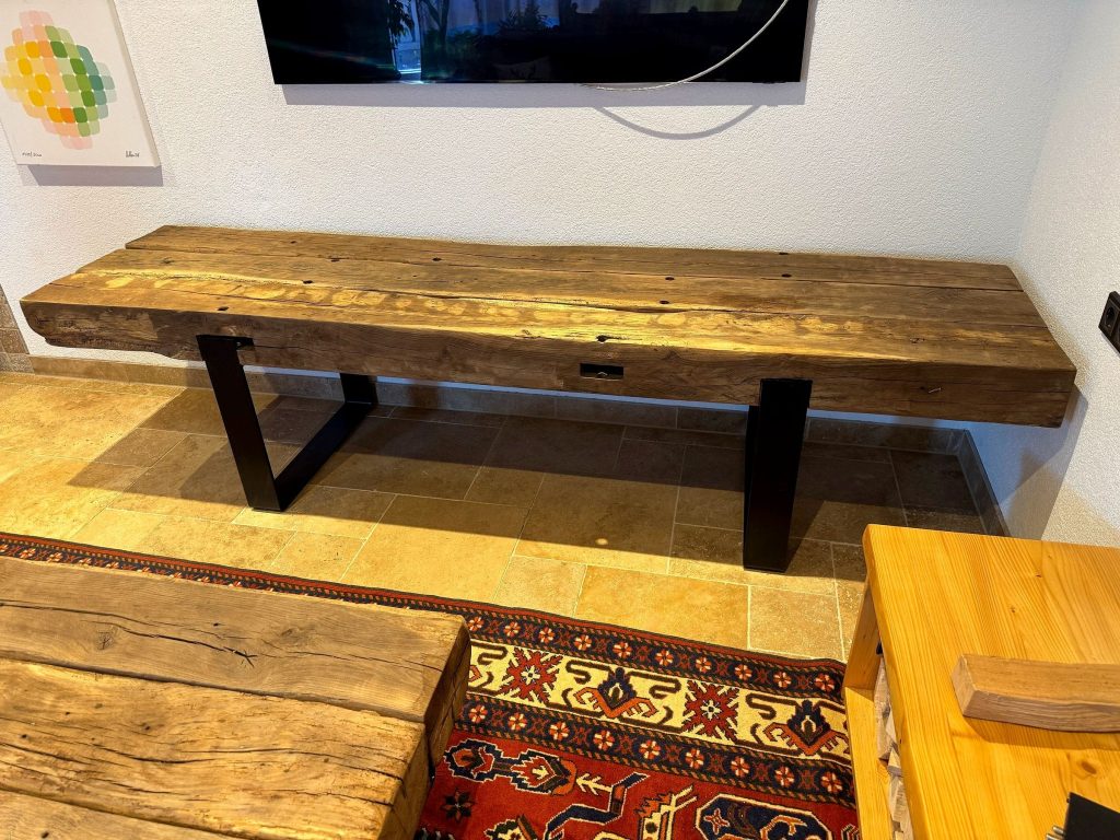 Balkenmöbel auf schwarzen Kufen vor einem Fernseher