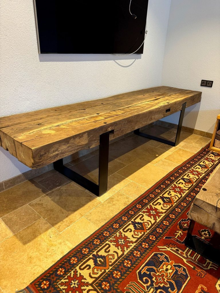 Massives Möbelstück aus alten Balken auf Stahlkufen in einem Wohnraum mit Teppich