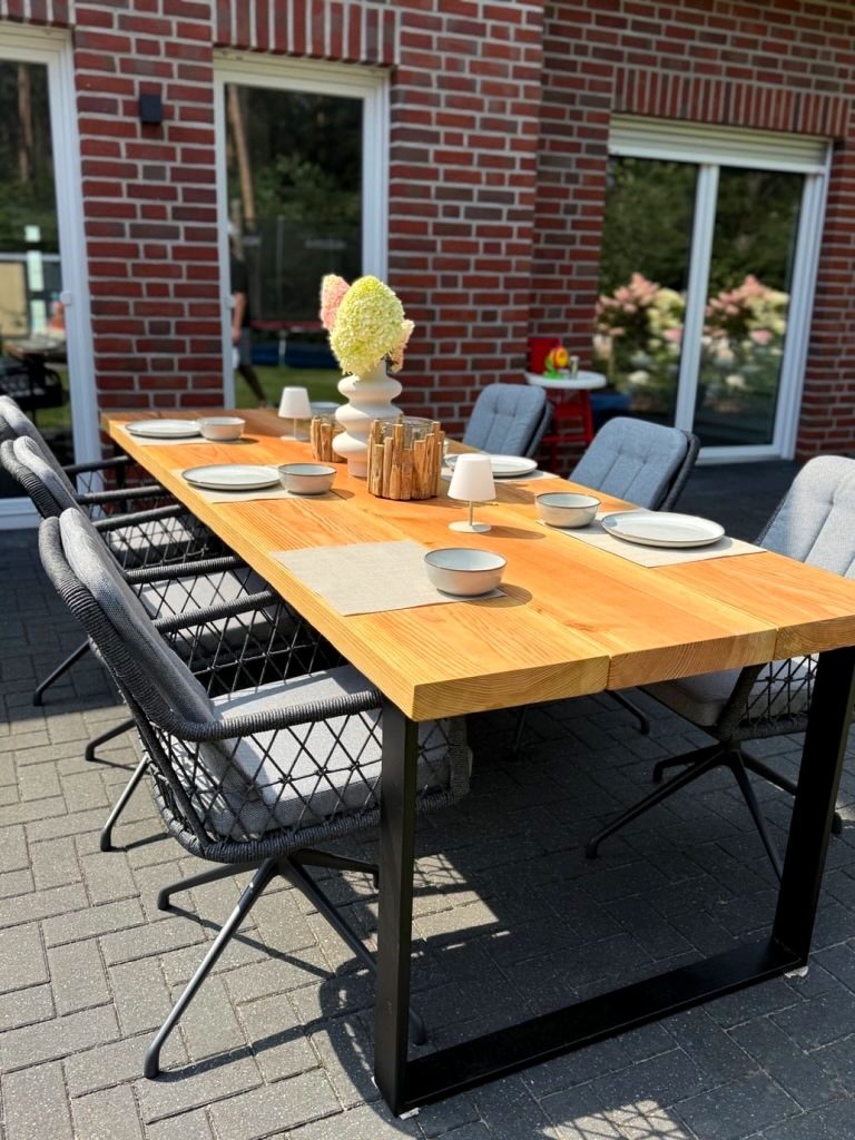 Gedeckter Esstisch aus hellen Holzbohlen auf schwarzem Stahlgestell auf einer Terrasse